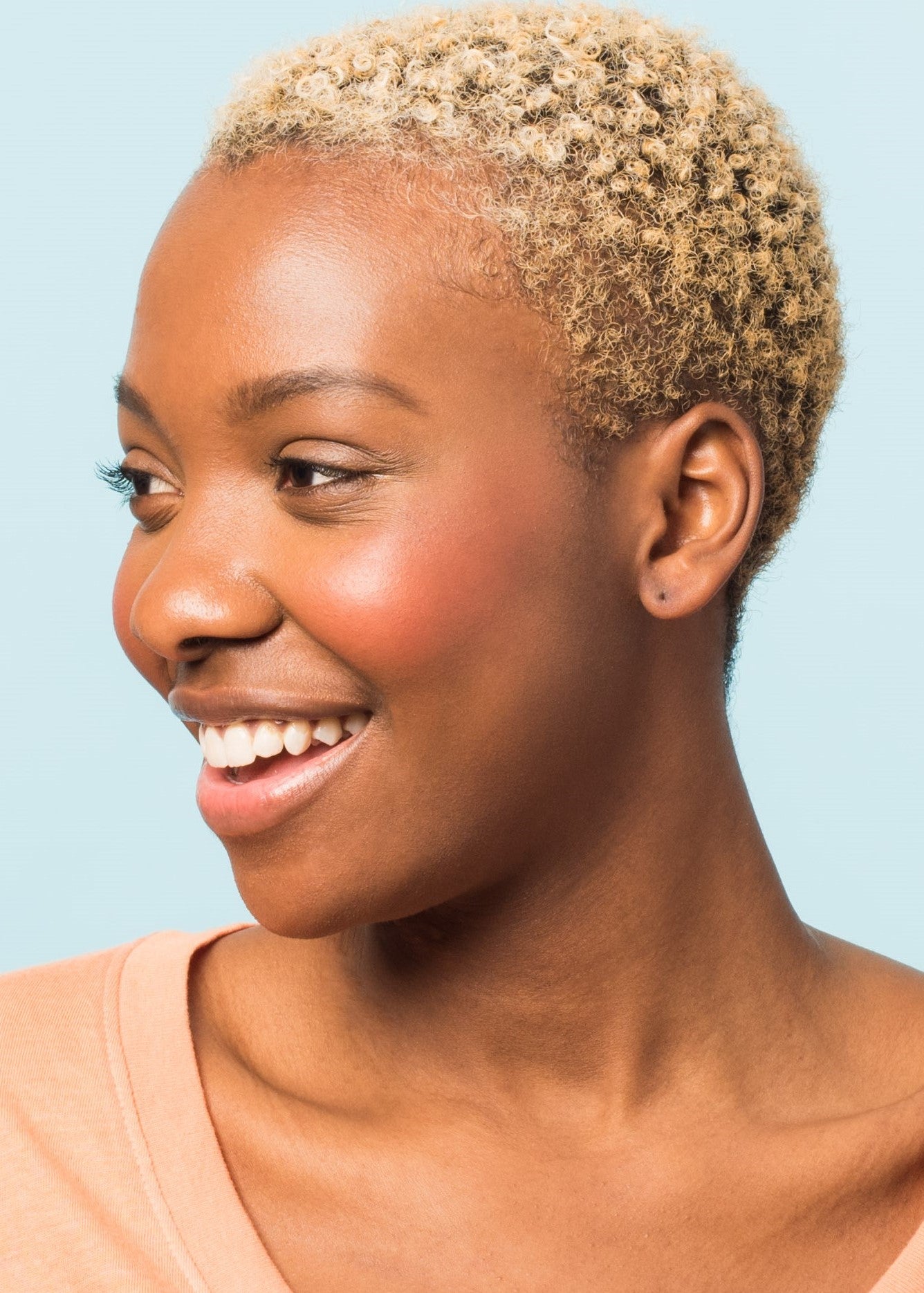 smiling girl showing her side cheek applied with cream blush in shade hot