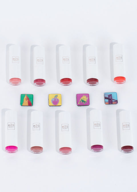 ten moisturizing lipsticks in different shades lying down in two horizontal lines with nyc themed blocks in the middle