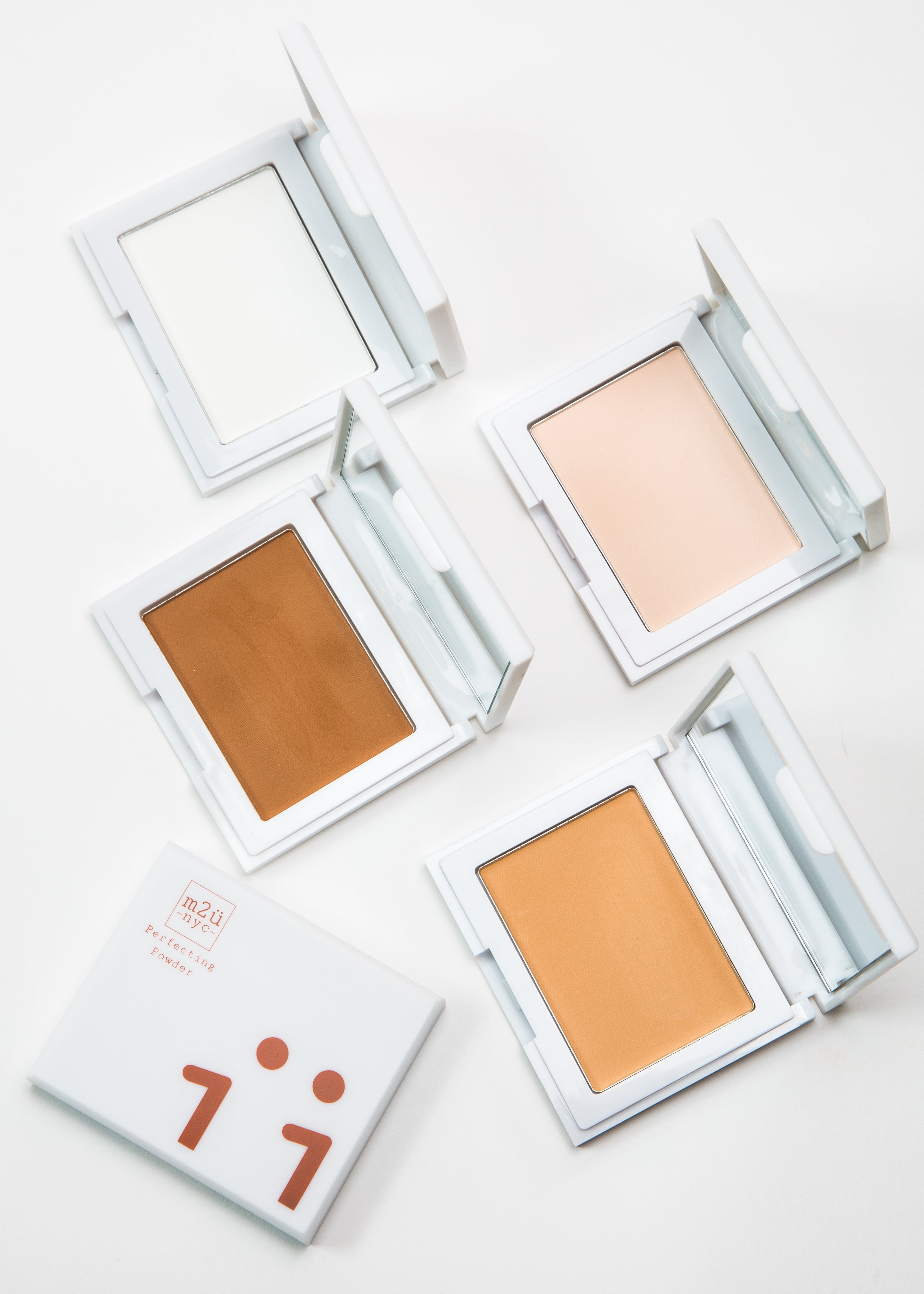 four open perfecting powder compacts in four shades with mirrors and one closed 