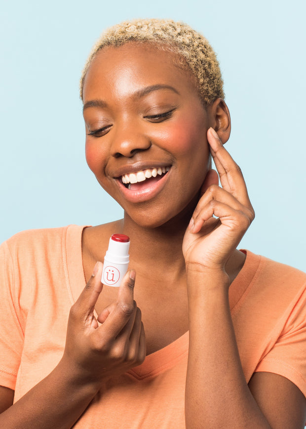 girl holding a cream blush stick applying profuct on face