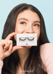 girl wearing false eyelashes holding a pair in a white box with red lips