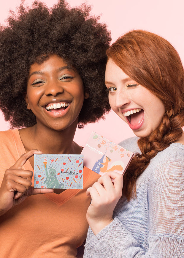 two girls holding different eyeshadow palettes with big smiles and a wink face