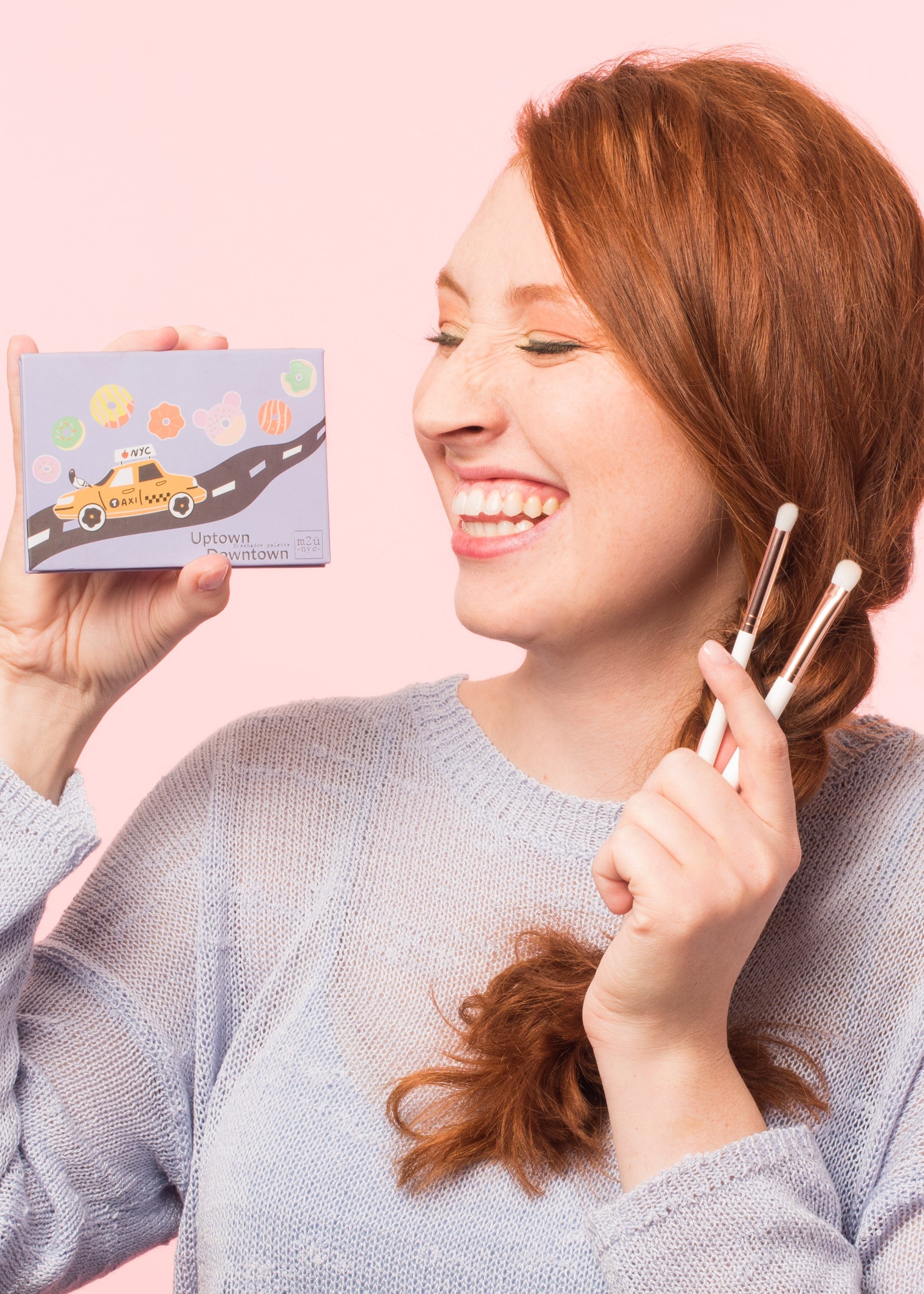 smiling girl holding an eyeshadow palette on one hand and the eyeshadow brush set on the other hand