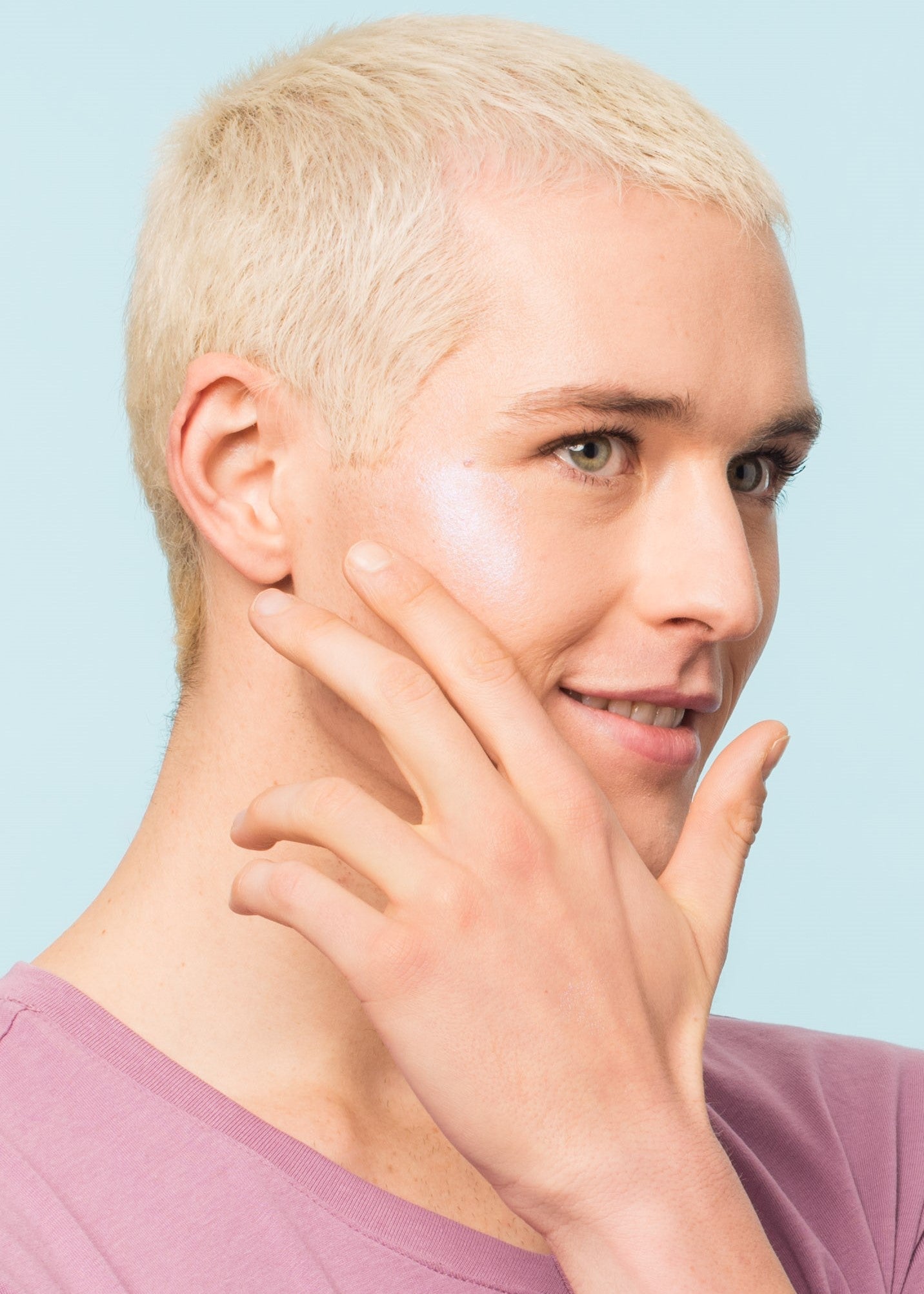man happily applying jelly highlighter on the right side of his cheek with fingers
