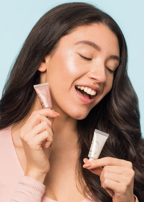 smiling girl looking down holding two tubes of liquid highlighter in two different shades