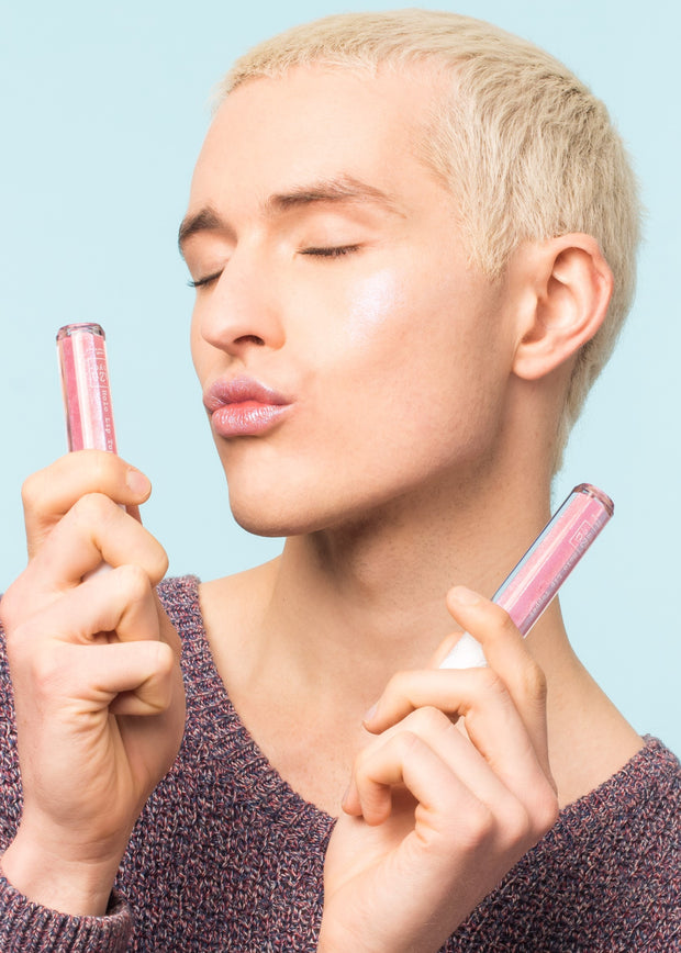 man holding two bottles of the holographic lip gloss air kissing the product with eyes closed