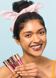 smiling girl wearing metallic liquid lip holding four bottles of metallic liquid lip in different shades