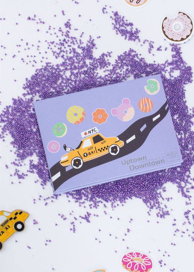 new york city inspired eyeshadow palette sitting among purple sprinkles, donuts and mini taxi